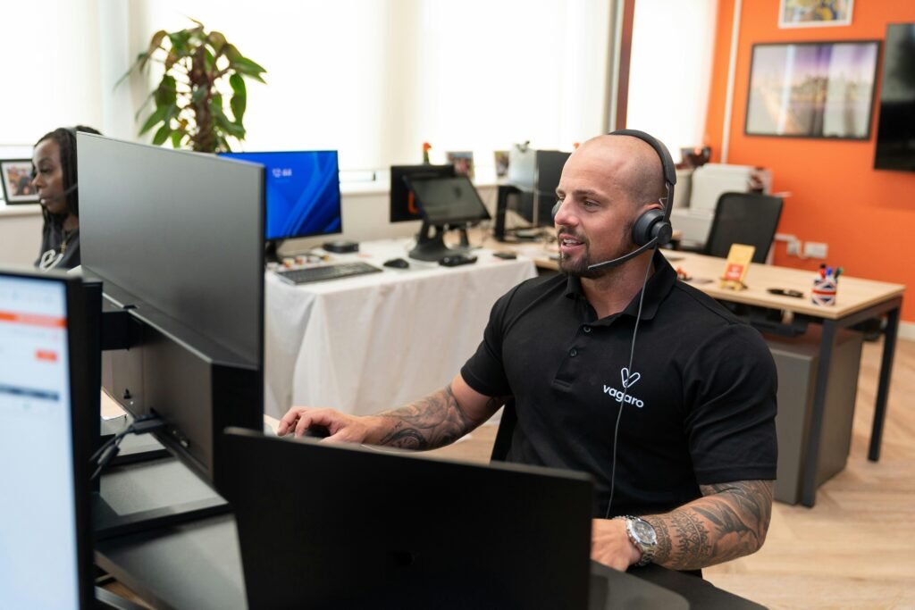 Ein Mann mit Headset sitzt an einem Schreibtisch vor einem Computer und arbeitet konzentriert im Büro.