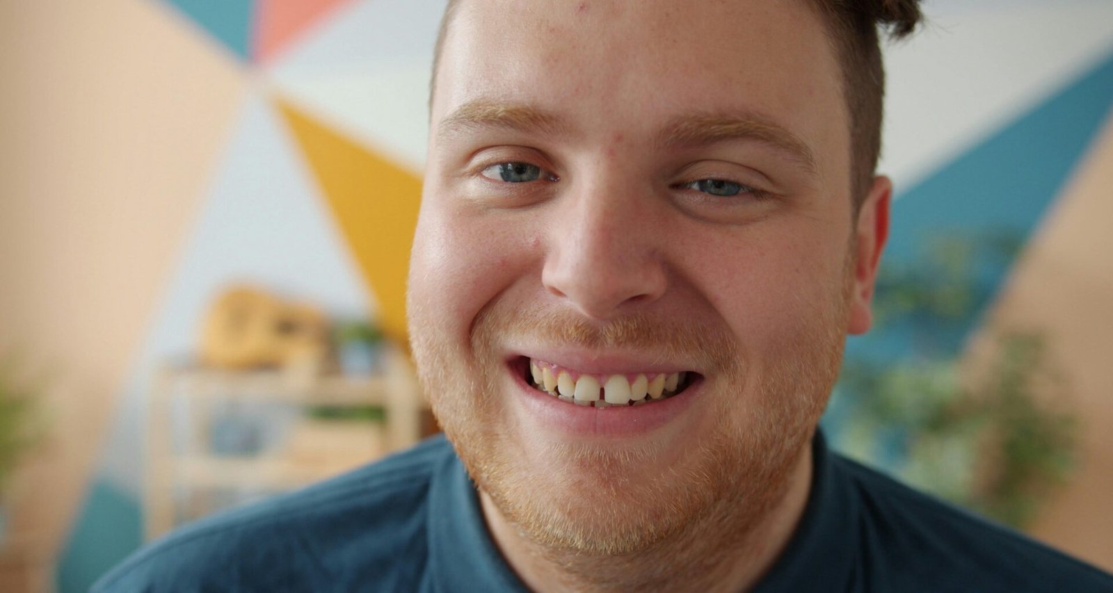 Ein Mann mit roten Haaren blickt lächelnd direkt in die Kamera, neutrale Kulisse, freundlicher Ausdruck