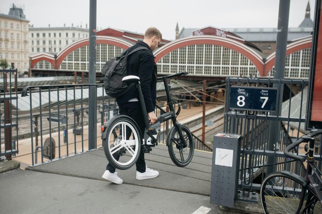 Mann mit Rucksack steht mit einem Fahrrad an einem Bahnsteig in einem Bahnhof. Moderne urbane Verkehrsszene.
