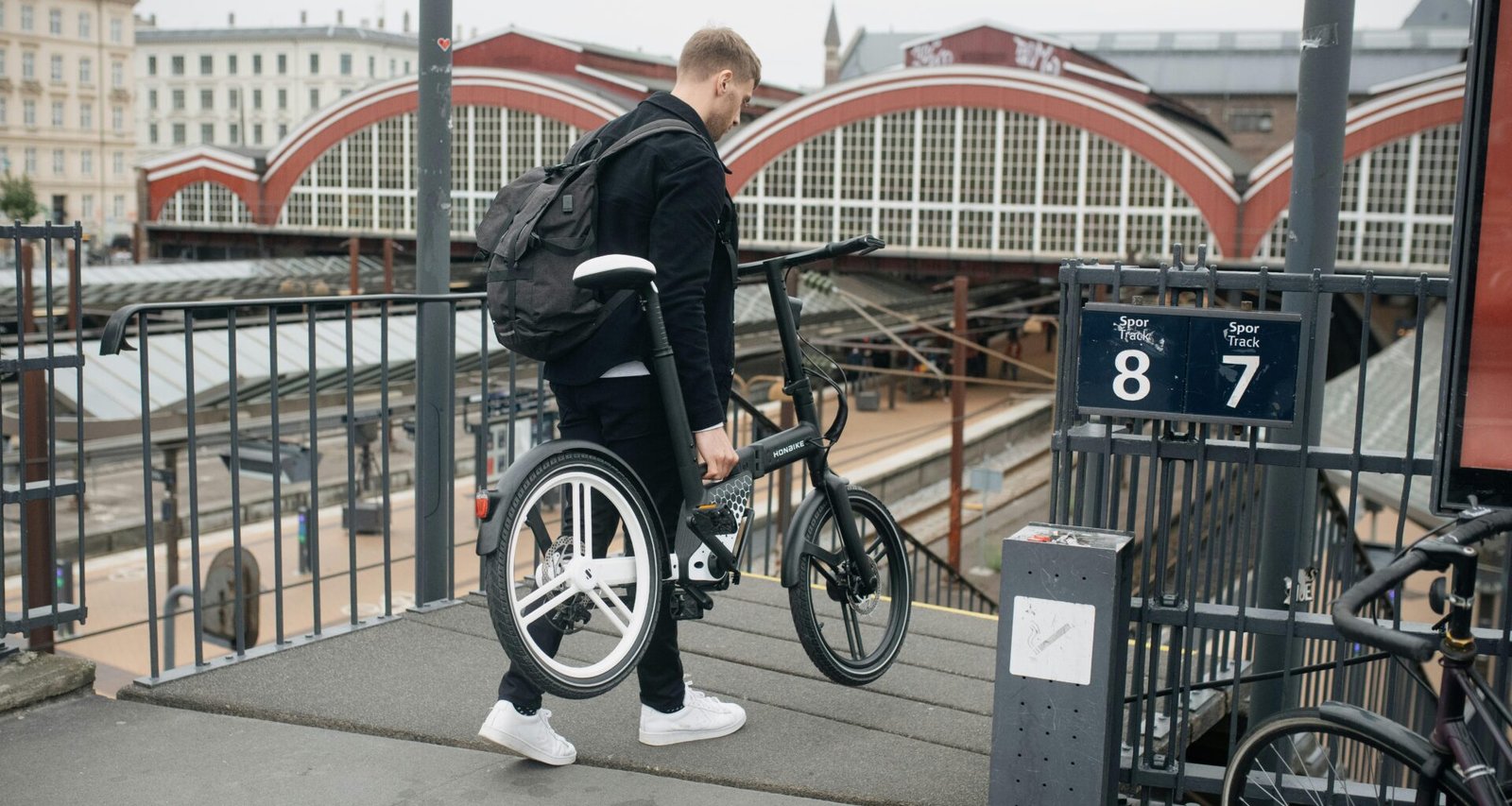 Mann mit Rucksack steht mit einem Fahrrad an einem Bahnsteig in einem Bahnhof. Moderne urbane Verkehrsszene.