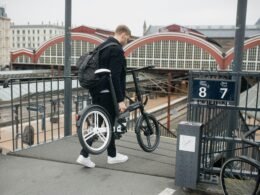 Mann mit Rucksack steht mit einem Fahrrad an einem Bahnsteig in einem Bahnhof. Moderne urbane Verkehrsszene.