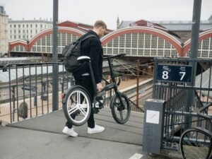 Mann mit Rucksack steht mit einem Fahrrad an einem Bahnsteig in einem Bahnhof. Moderne urbane Verkehrsszene.
