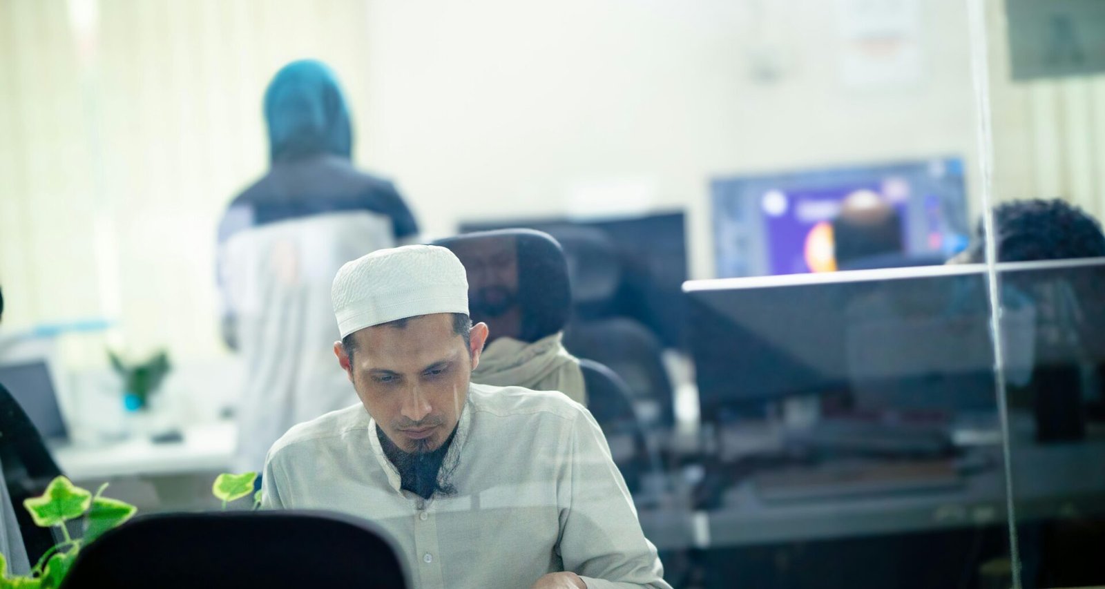 Mann sitzt an einem Schreibtisch im hellen Büro mit Laptop und Büromaterialien, moderne Arbeitsumgebung