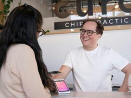 Ein Mann sitzt an einem Schreibtisch und spricht mit einer Frau in einem modernen Büro. Thematisch geeignet für Arbeitswelt- oder Kommunikationsthemen.