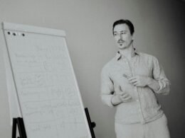 Ein Mann steht neben einem Whiteboard mit verschiedenen Notizen, ideal für Artikel über Teamarbeit oder Strategieplanung.