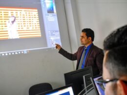 Ein Mann steht vor einer Projektionsleinwand und spricht während einer Präsentation zu seinem Publikum.