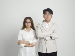 Ein Mann und eine Frau stehen nebeneinander und schauen gemeinsam in eine Richtung, beide im Business-Outfit.