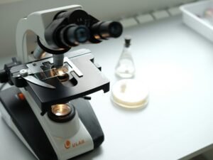 Ein Mikroskop steht auf einem Labortisch neben einer Flasche, symbolisiert Forschung und wissenschaftliche Arbeit.