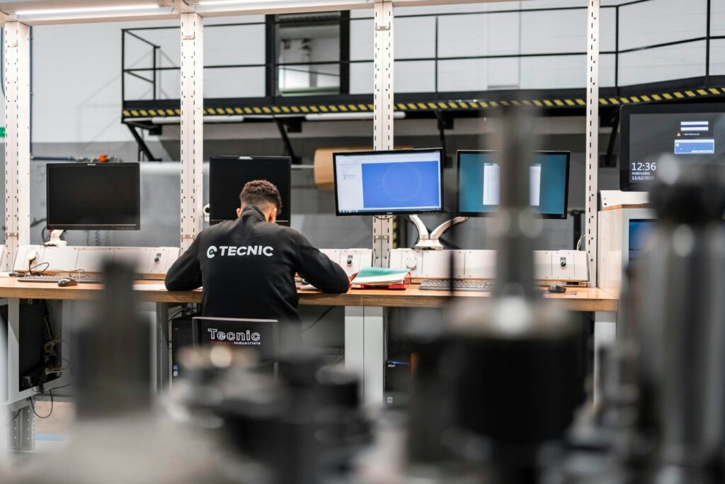 Ein Mitarbeiter sitzt an einem Schreibtisch und arbeitet konzentriert vor mehreren Computerbildschirmen im Büro.