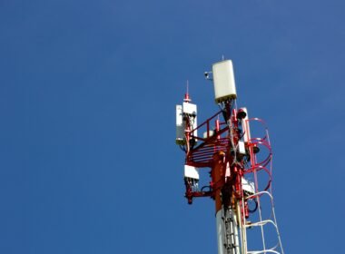 Ein Mobilfunkmast vor blauem Himmel steht im Mittelpunkt und repräsentiert zeitgemäße Kommunikationstechnologien.