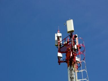 Ein Mobilfunkmast vor blauem Himmel steht im Mittelpunkt und repräsentiert zeitgemäße Kommunikationstechnologien.