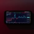 Ein Mobiltelefon mit einer Börsenchart-Anzeige vor einem roten Hintergrund, Finanztechnologie und mobiles Trading dargestellt.