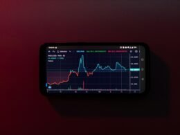 Ein Mobiltelefon mit Aktienchart auf dem Display vor rotem Hintergrund, das mobile Finanzanalyse darstellt