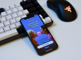 Ein Mobiltelefon liegt unmittelbar neben einer Computer-Tastatur auf einem Schreibtisch in einer Büroumgebung.