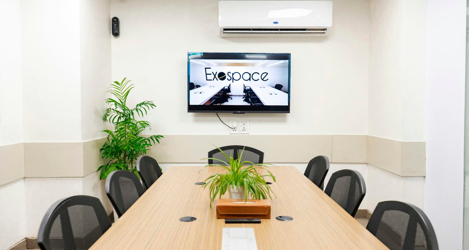 Heller Konferenzraum mit großem Tisch, mehreren Stühlen und einem an der Wand montierten Fernseher im modernen Design.