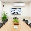 Heller, moderner Konferenzraum mit großem Fernseher, Tisch und mehreren Stühlen, ideal für Meetings und Präsentationen.