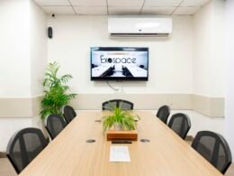 Heller, moderner Konferenzraum mit großem Fernseher, Tisch und mehreren Stühlen, ideal für Meetings und Präsentationen.