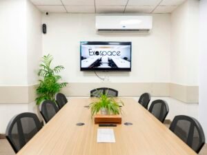 Heller, moderner Konferenzraum mit großem Fernseher, Tisch und mehreren Stühlen, ideal für Meetings und Präsentationen.