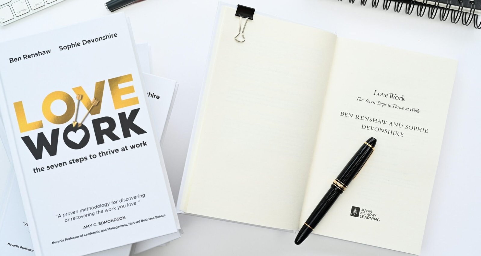 Ein aufgeklapptes Notizbuch mit einem Stift darauf neben einer Computertastatur auf einem Schreibtisch