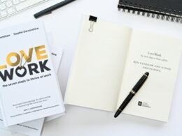 Ein aufgeklapptes Notizbuch mit einem Stift darauf neben einer Computertastatur auf einem Schreibtisch