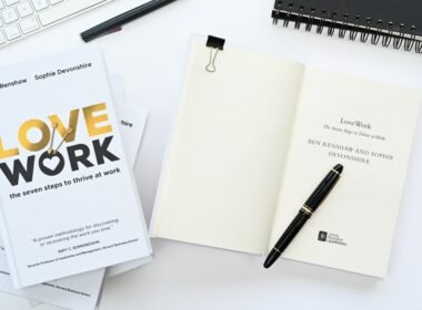 Ein aufgeklapptes Notizbuch mit einem Stift darauf neben einer Computertastatur auf einem Schreibtisch