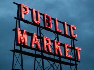 Ein großes, beleuchtetes Schild mit der Aufschrift 'Public Market' leuchtet nachts über einem städtischen Markt.