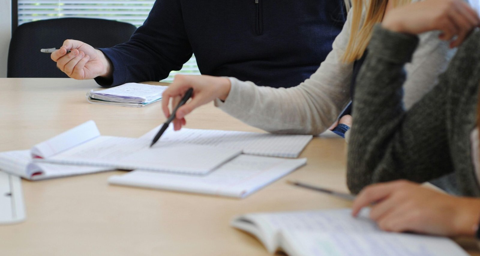 Mehrere Menschen sitzen an einem Tisch und arbeiten zusammen an Laptops in einem modernen Arbeitsumfeld.