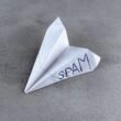 Ein Papierflieger mit dem Wort Spam darauf, symbolisiert unerwünschte E-Mail-Nachrichten im digitalen Marketing.