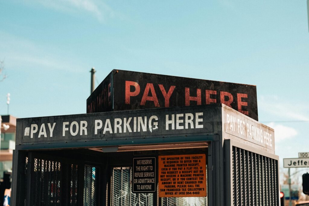 Ein weißes „Pay Here“-Schild mit schwarzer Schrift steht auf dem Dach eines Gebäudes und weist auf eine Zahlstation hin.