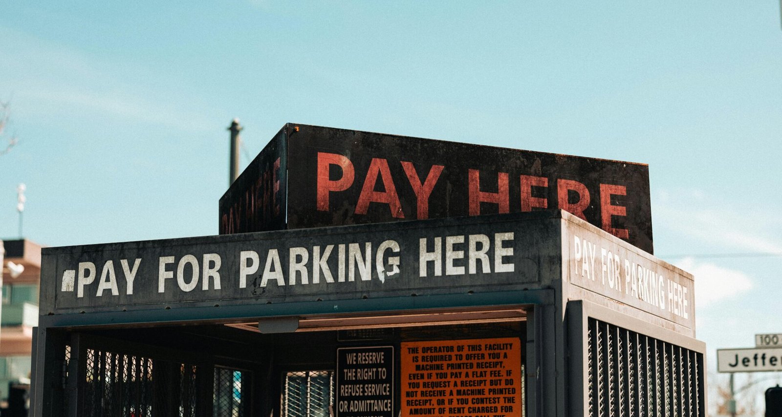 Ein weißes „Pay Here“-Schild mit schwarzer Schrift steht auf dem Dach eines Gebäudes und weist auf eine Zahlstation hin.