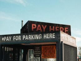 Ein weißes „Pay Here“-Schild mit schwarzer Schrift steht auf dem Dach eines Gebäudes und weist auf eine Zahlstation hin.