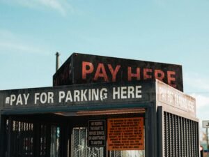 Ein weißes „Pay Here“-Schild mit schwarzer Schrift steht auf dem Dach eines Gebäudes und weist auf eine Zahlstation hin.