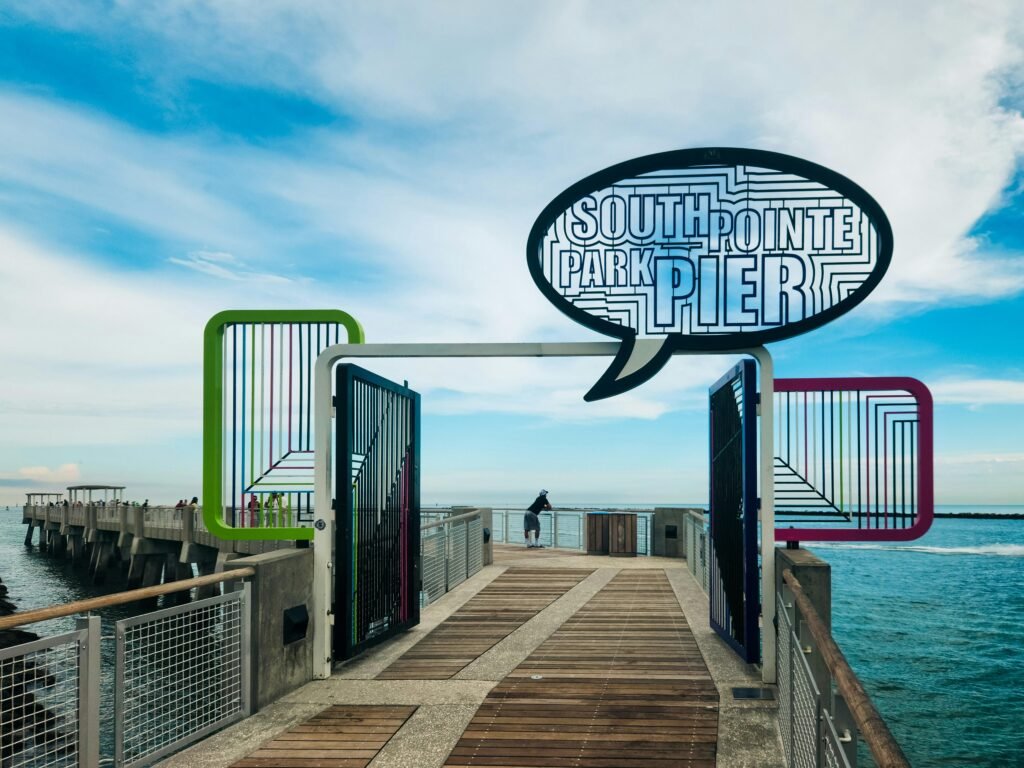 Ein langer Pier mit einem Hinweisschild 'South Point Pier', der gerade ins Meer hineinragt, bei Tageslicht fotografiert