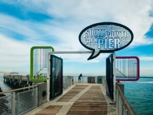 Ein langer Pier mit einem Hinweisschild 'South Point Pier', der gerade ins Meer hineinragt, bei Tageslicht fotografiert
