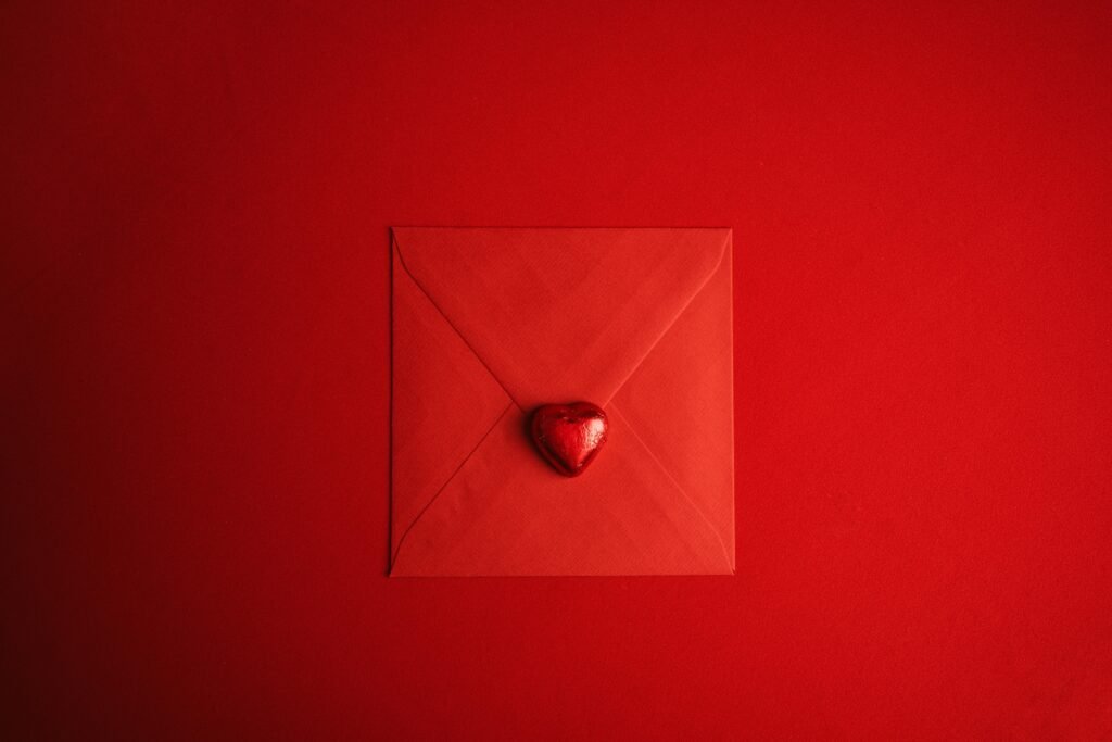 Roter Umschlag mit einem Herzsymbol in der Mitte, fotografiert auf hellem Untergrund, geeignet für Themen zur digitalen Kommunikation