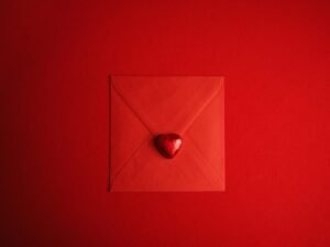 Roter Umschlag mit einem Herzsymbol in der Mitte, fotografiert auf hellem Untergrund, geeignet für Themen zur digitalen Kommunikation