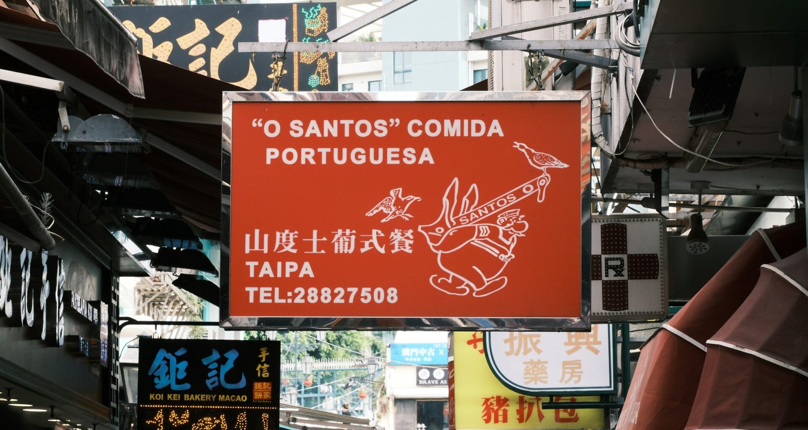 Rotes Schild hängt seitlich an einem Gebäude in städtischer Umgebung, aufgenommen von Luka auf Unsplash