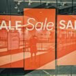 Schaufenster eines Geschäfts mit auffälligem Sale-Schild und reflektierender Glasfront in einer Einkaufsstraße