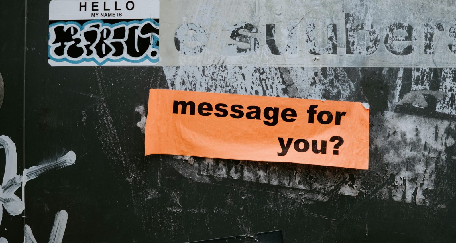 Ein Schild mit der Aufschrift 'Message for you?' ist an einer grauen Wand befestigt und thematisiert Kommunikation.