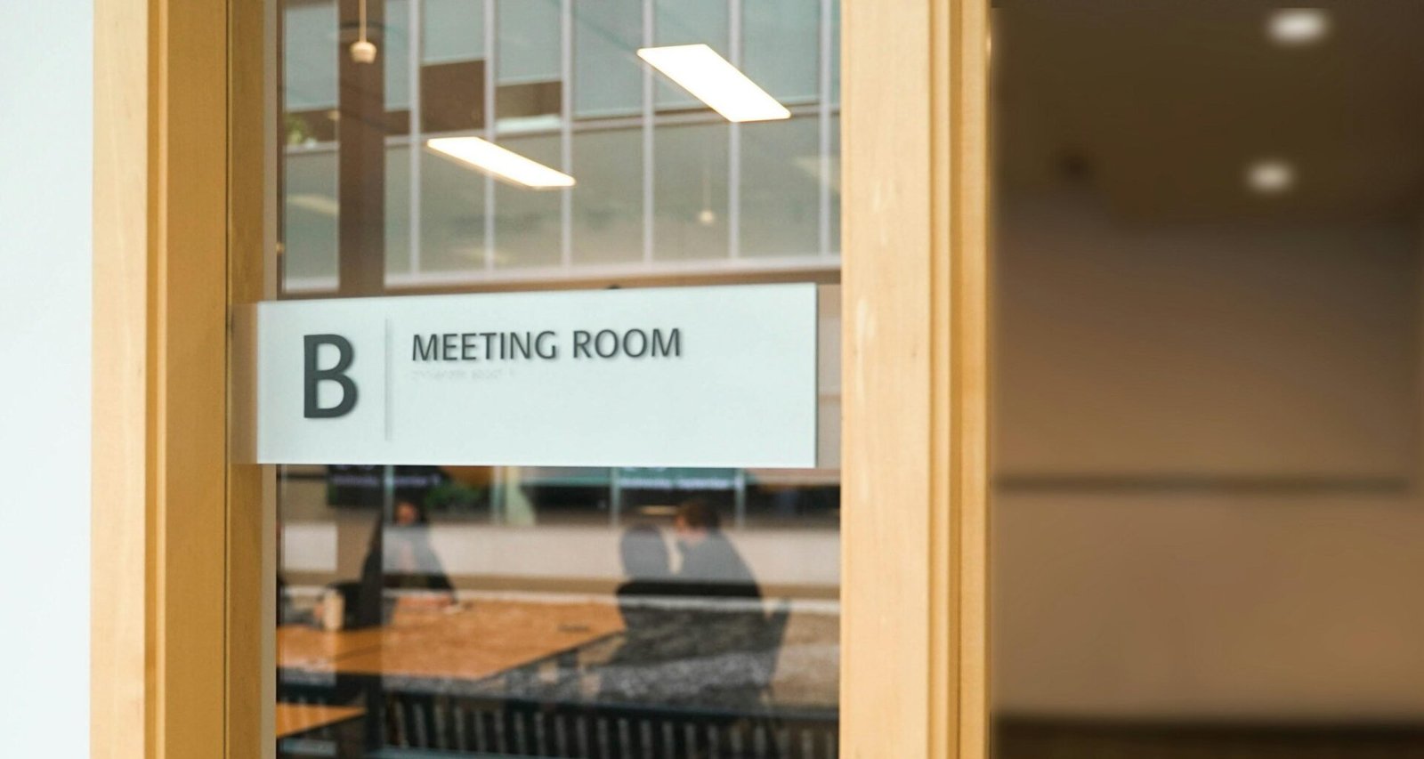 Ein Schild mit der Aufschrift Meeting Room hängt an einer Glastür und kennzeichnet einen Besprechungsraum in einem modernen Büro.
