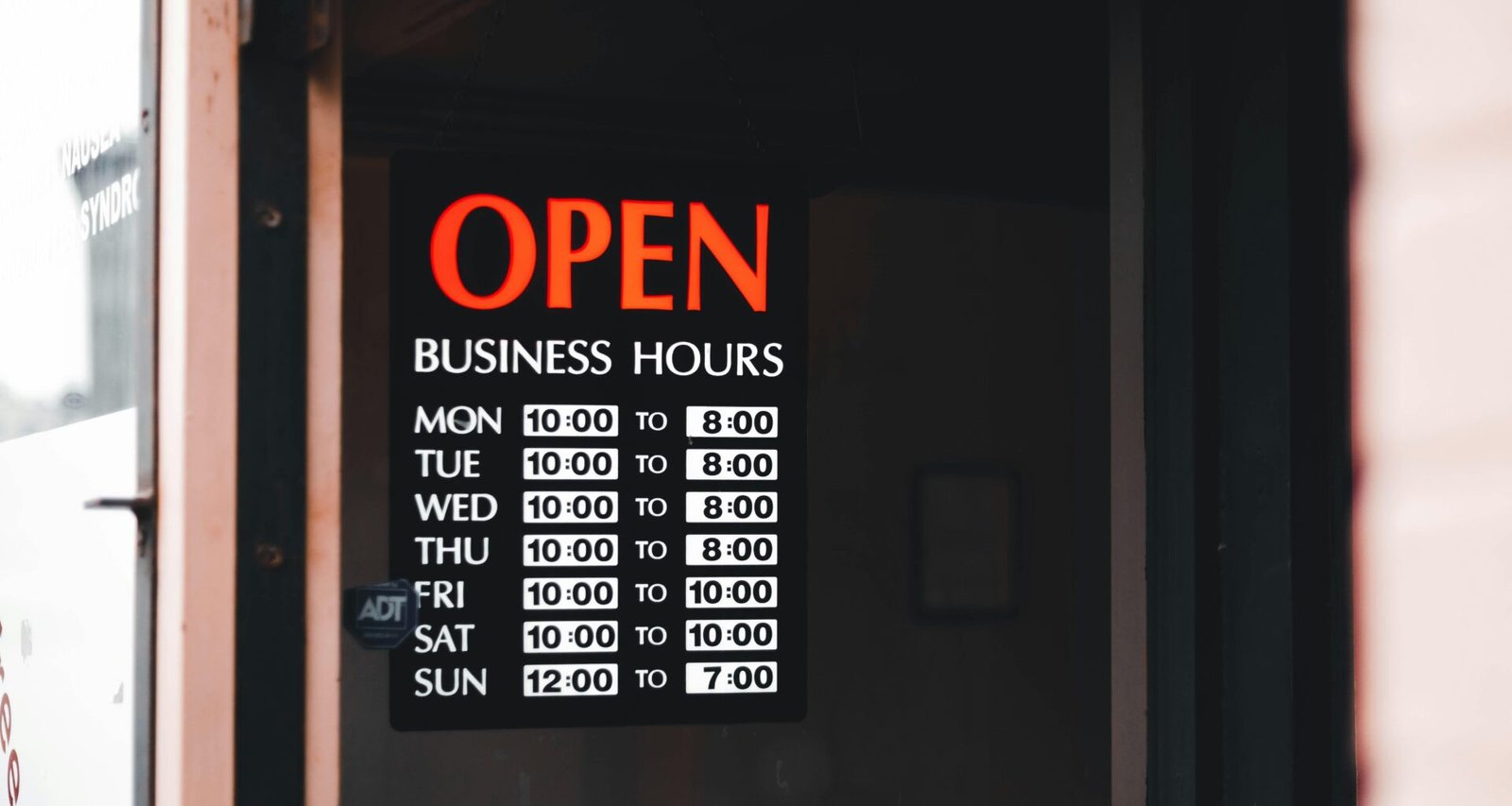 Tür mit einem Schild, das auf die aktuellen Öffnungszeiten eines Geschäfts hinweist, englischer Text: Open Business Hours