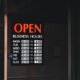 Tür mit einem Schild, das auf die aktuellen Öffnungszeiten eines Geschäfts hinweist, englischer Text: Open Business Hours