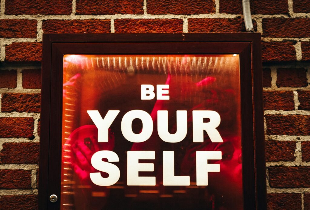Schild mit der Aufschrift Be Yourself angebracht an einer roten Backsteinwand, aufgenommen von Jon Tyson auf Unsplash