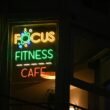 Ein beleuchtetes Fitness-Café Schild bei Nacht, das den Eingang und das Logo deutlich hervorhebt