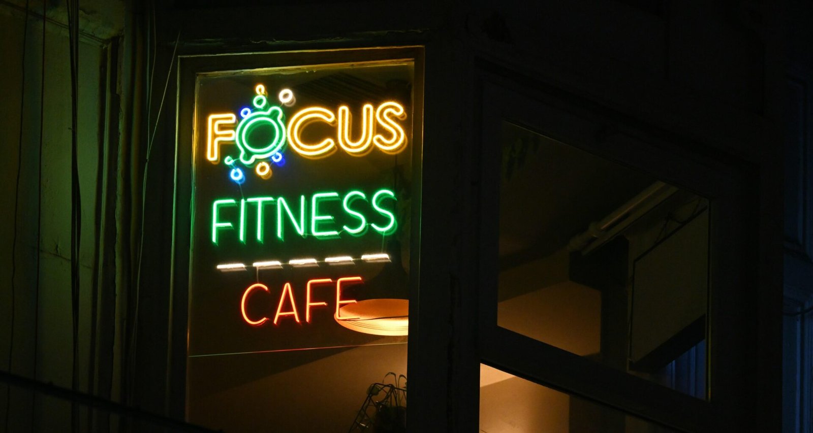 Ein beleuchtetes Fitness-Café Schild bei Nacht, das den Eingang und das Logo deutlich hervorhebt