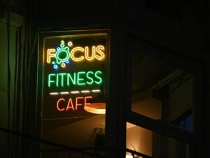 Ein beleuchtetes Fitness-Café Schild bei Nacht, das den Eingang und das Logo deutlich hervorhebt