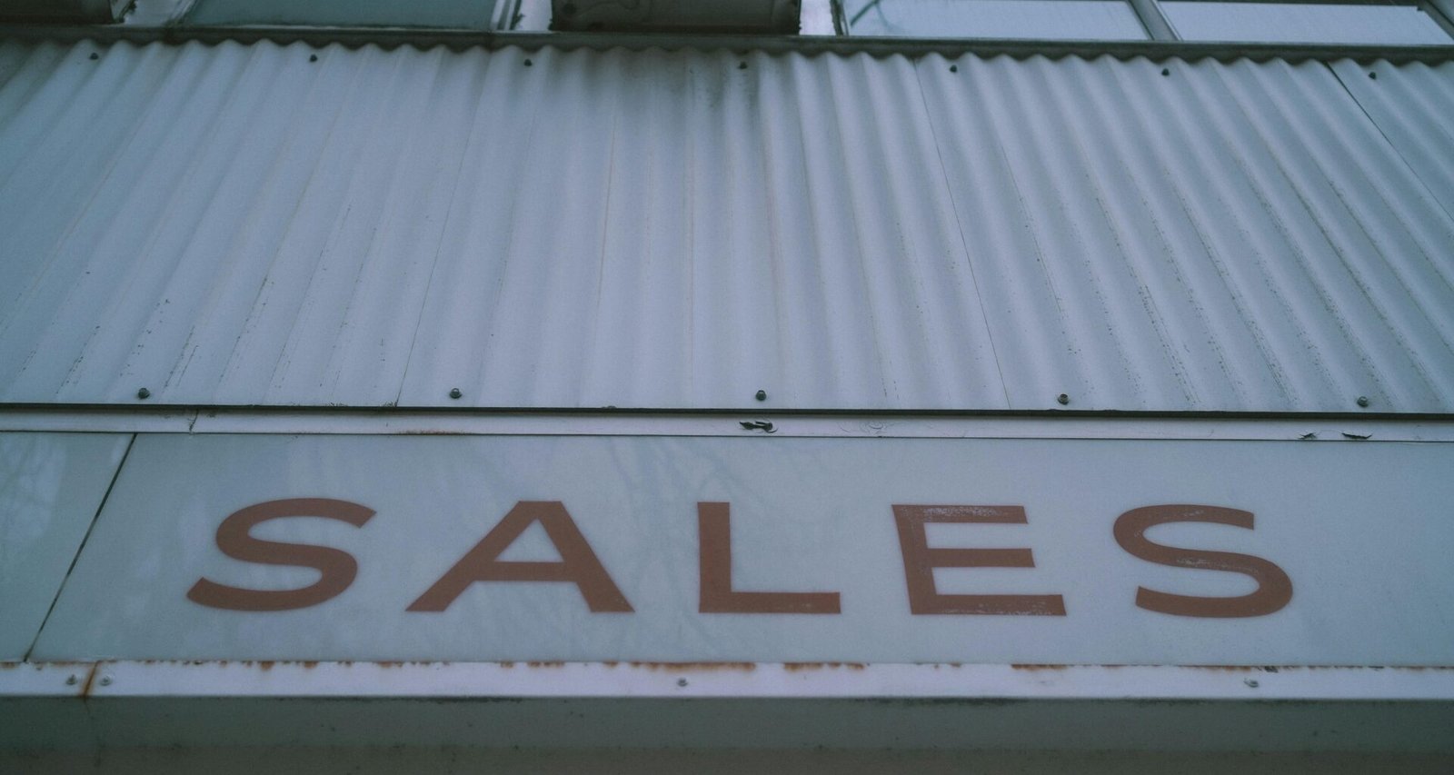 Ein rotes Verkaufsschild mit Aufschrift 'Sales' ist deutlich an der Außenwand eines Gebäudes angebracht.