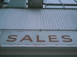 Ein rotes Verkaufsschild mit Aufschrift 'Sales' ist deutlich an der Außenwand eines Gebäudes angebracht.