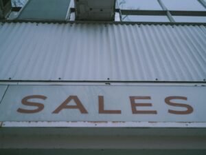 Ein rotes Verkaufsschild mit Aufschrift 'Sales' ist deutlich an der Außenwand eines Gebäudes angebracht.