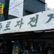 Ein Schild mit koreanischem Text hängt über dem Eingang eines Geschäfts und hebt die typische Beschilderung koreanischer Läden hervor.